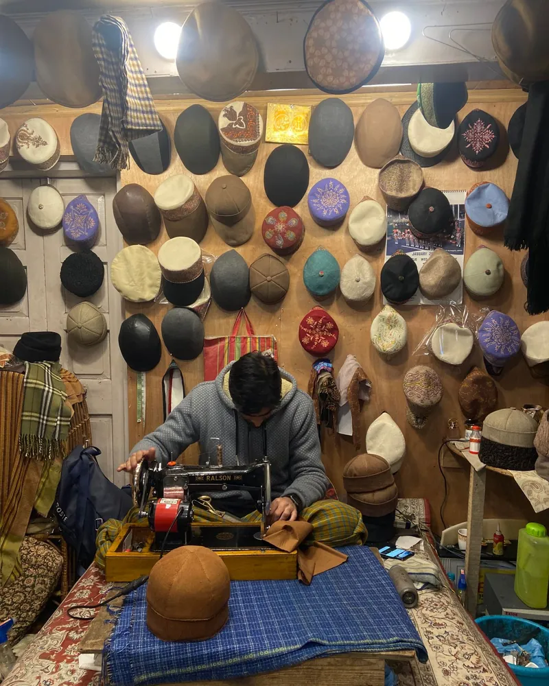 Interior de un taller de sombrerería con gorros de fieltro y textil colgados en la pared y una máquina de coser sobre la mesa de trabajo