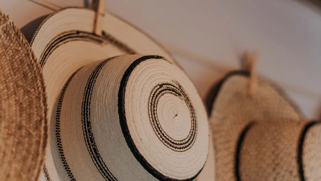 Sombreros de paja trenzada colgados en fila sobre una pared clara de taller